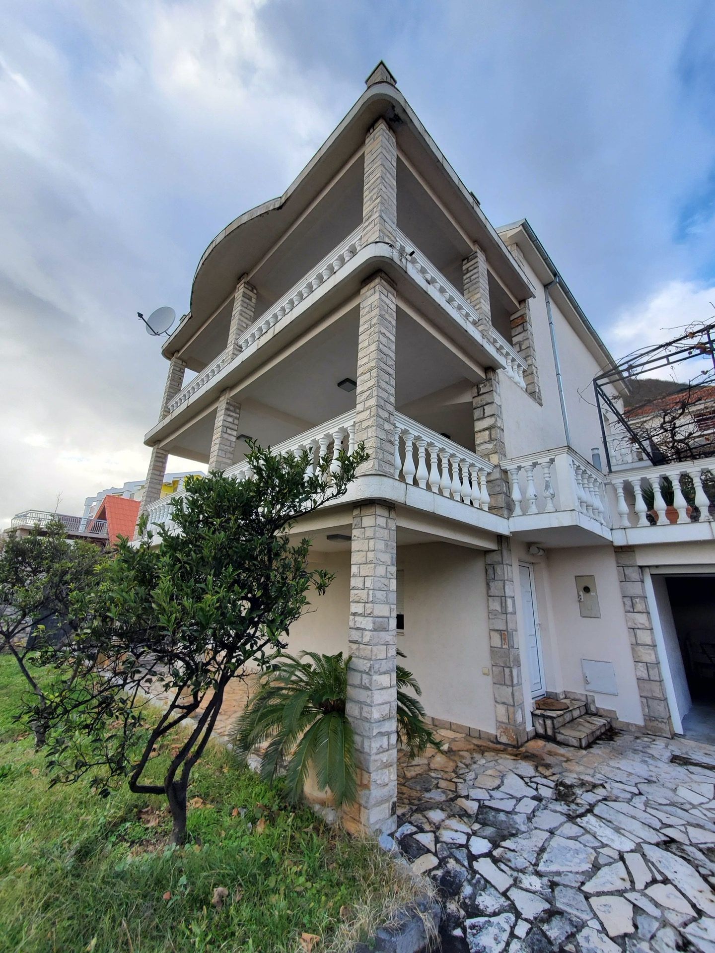 Three-story hotel in Bijela, Montenegro: facade with stone cladding, spacious terraces, and balustrades.