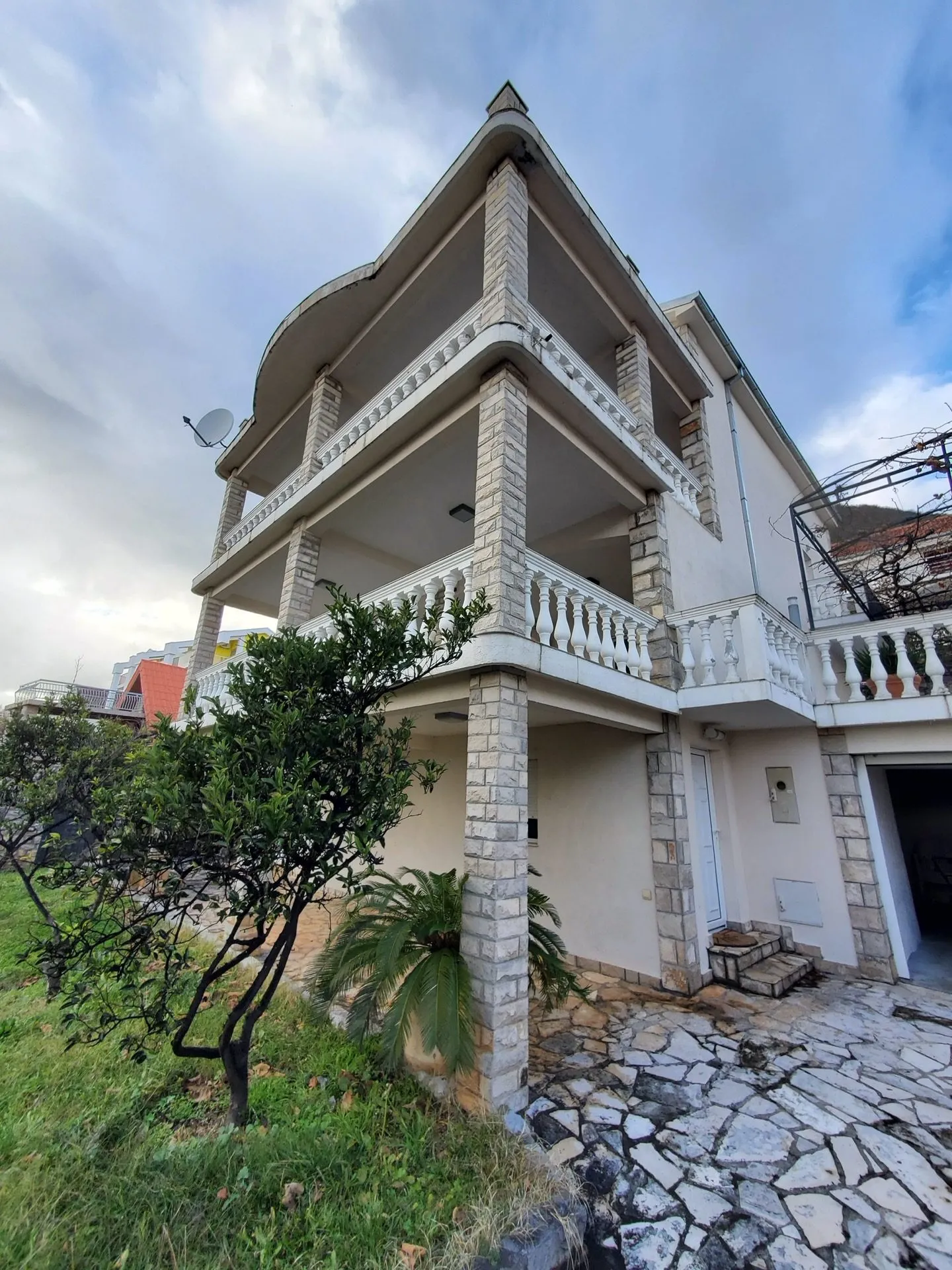 Exterior view of a two-story house featuring stone columns, white balustrades, and an irregular stone pathway in the foreground.