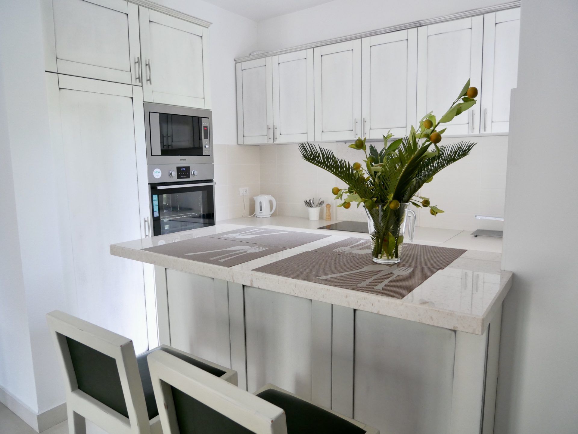 Modern white kitchen with a breakfast bar and built-in appliances in an apartment, Morinj, Montenegro.