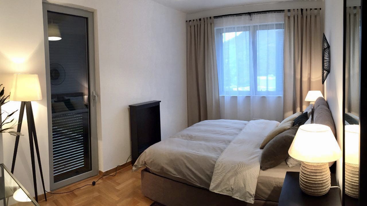 Cozy bedroom with a double bed in an apartment in Morinj, Montenegro: modern interior, parquet flooring, and a view from the window.