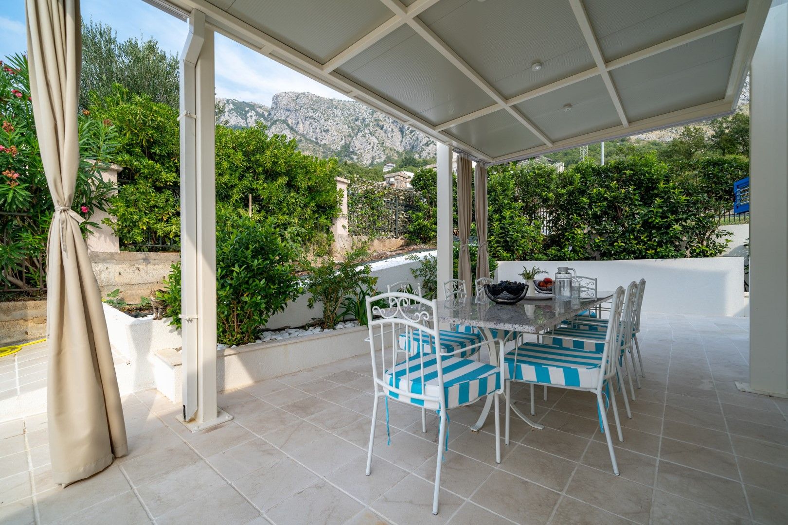 Covered terrace with dining area and mountain view in a house, Blizikuće, Montenegro. Garden furniture with striped cushions.