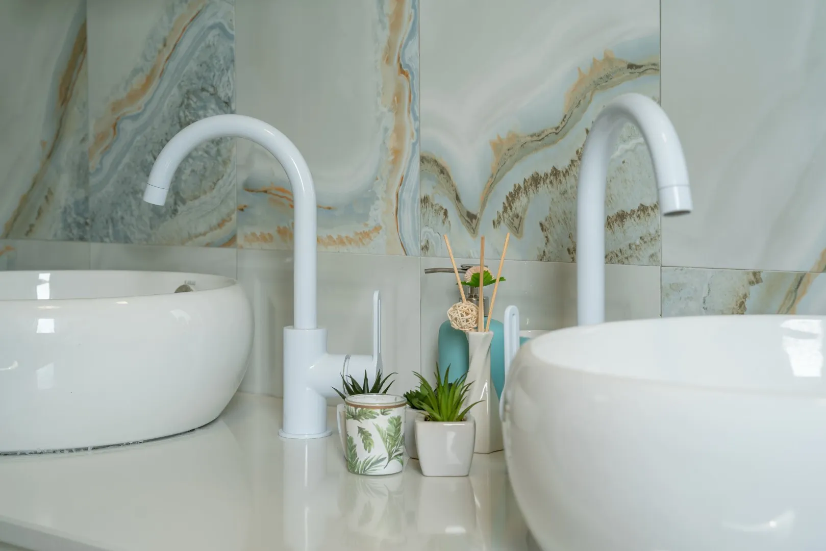 Two white vessel sinks with tall white faucets against a decorative marble-patterned tile wall.