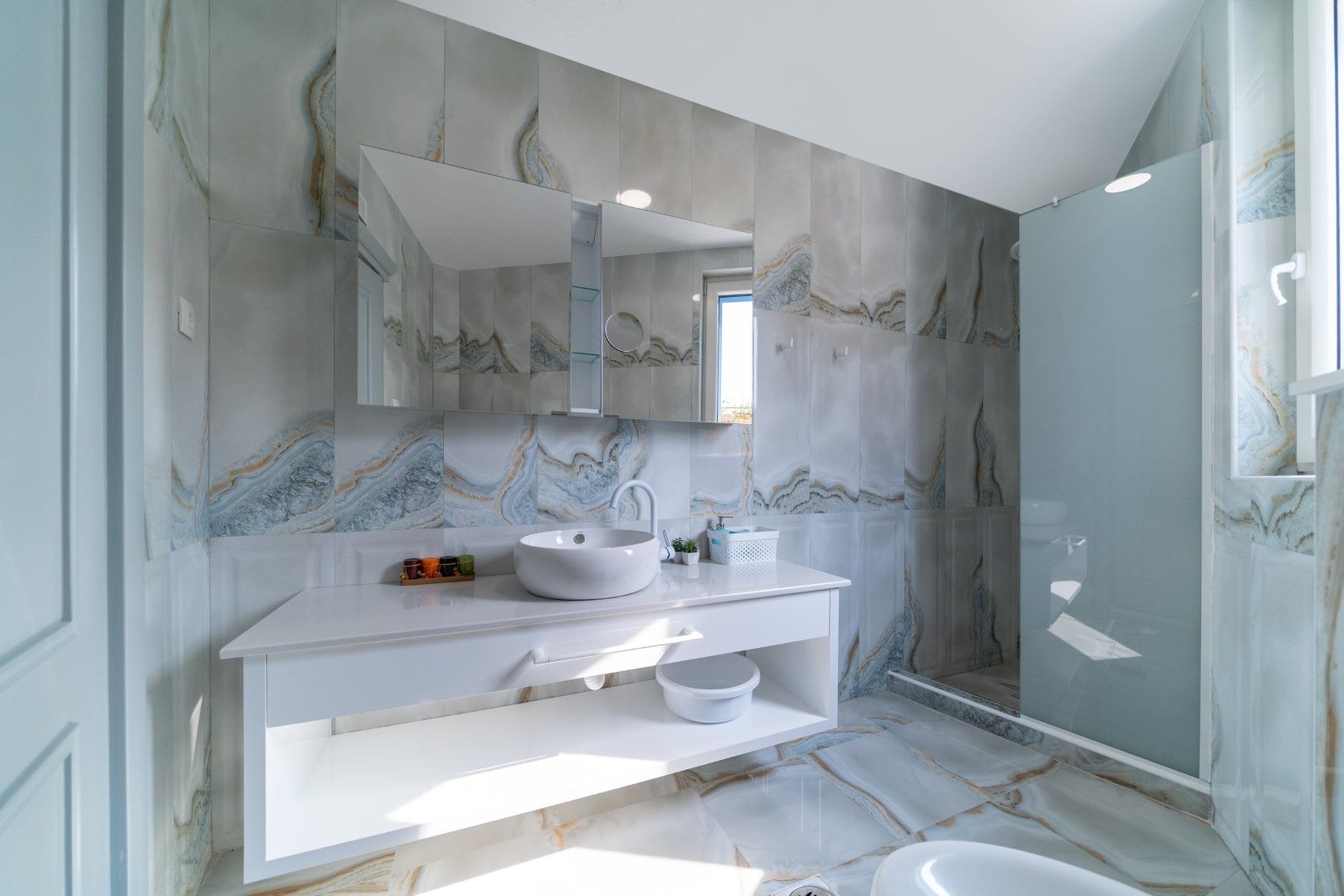 Modern bathroom with marble-look finishes in a house, Blizikuće, Montenegro: white vanity, sink, and shower cabin.