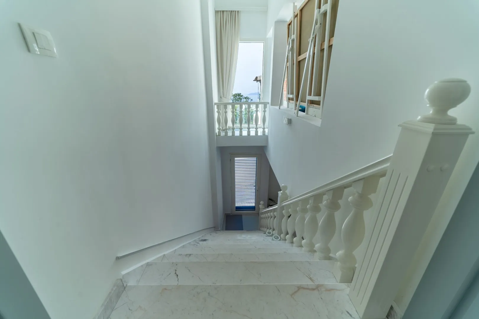 White marble staircase with balustrade, looking down to a lower level and balcony railing.