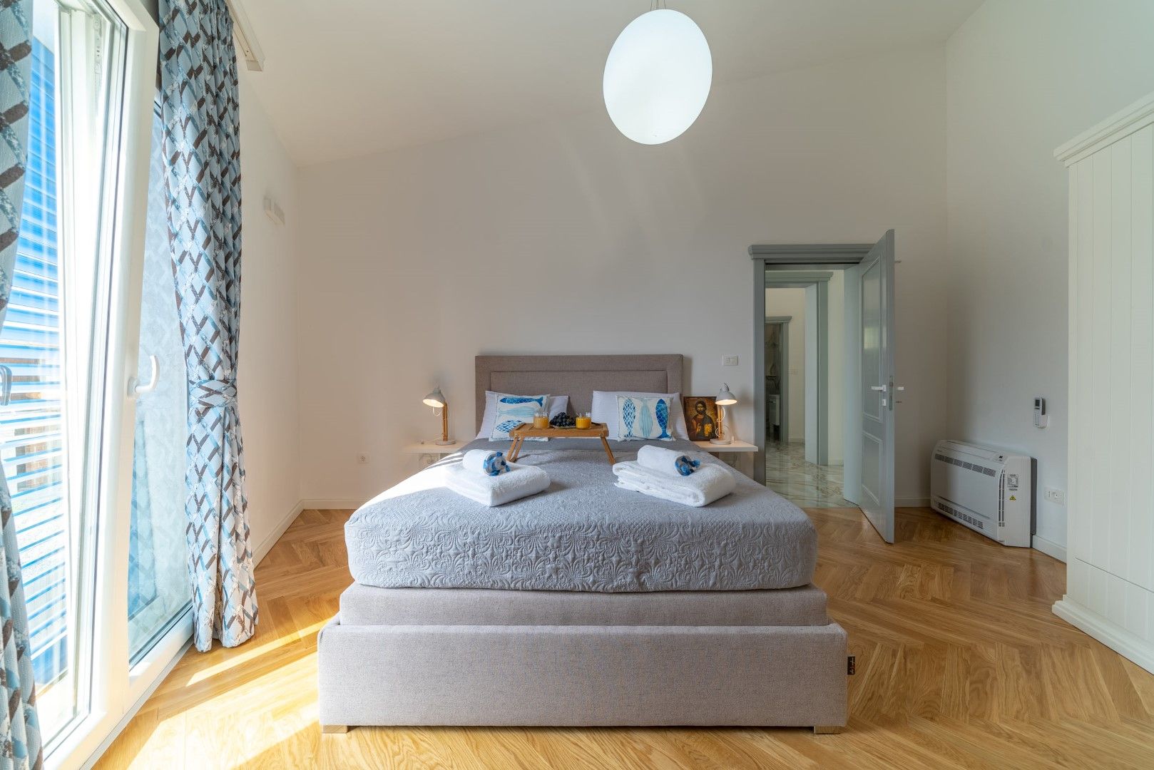 Bright bedroom with a double bed and parquet flooring in a house, Blizikuće, Montenegro. Interior view with access to the balcony.