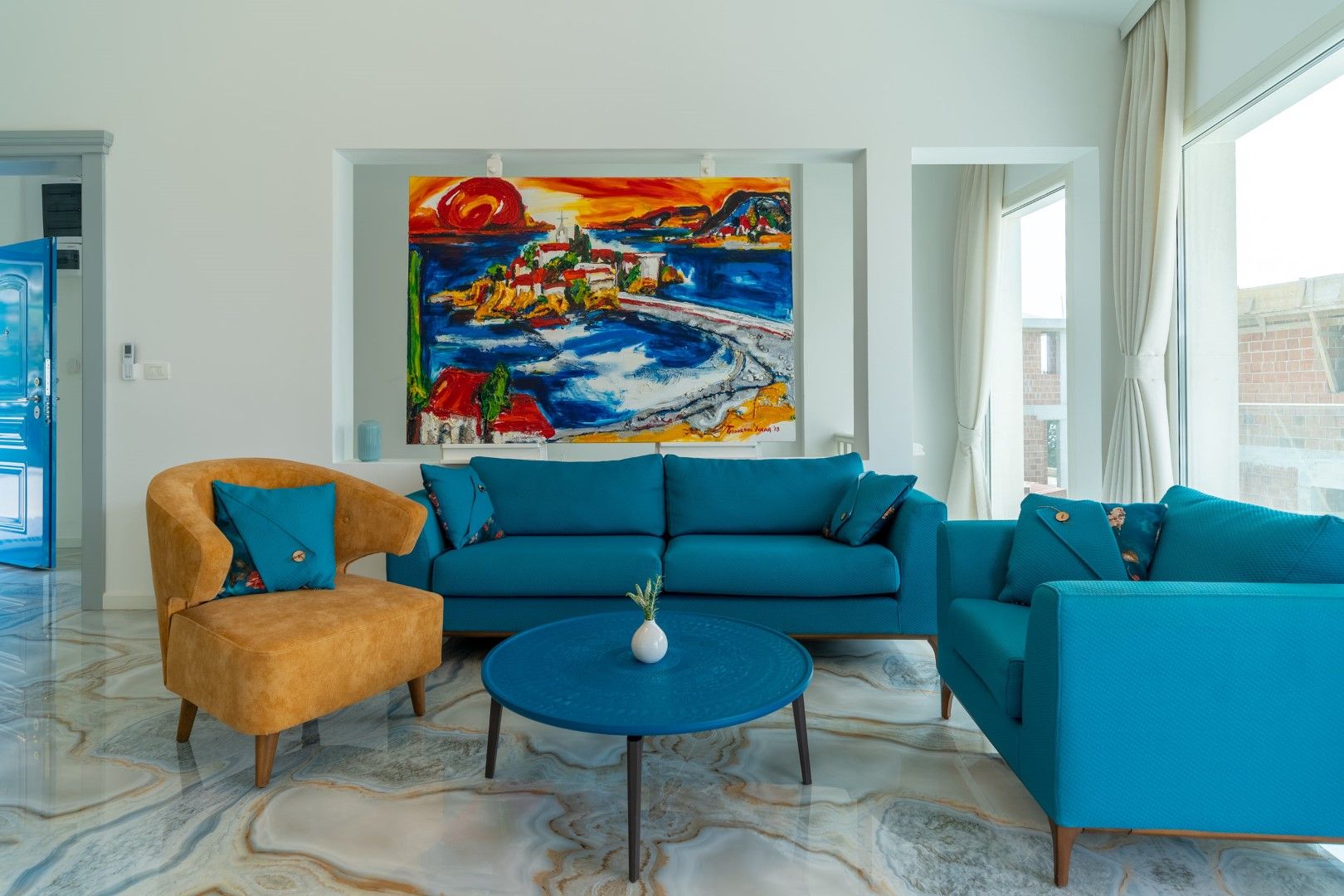 Living room in a house in Blizikuće, Montenegro: bright furniture, marble floor, and a painting with a view of Sveti Stefan island.