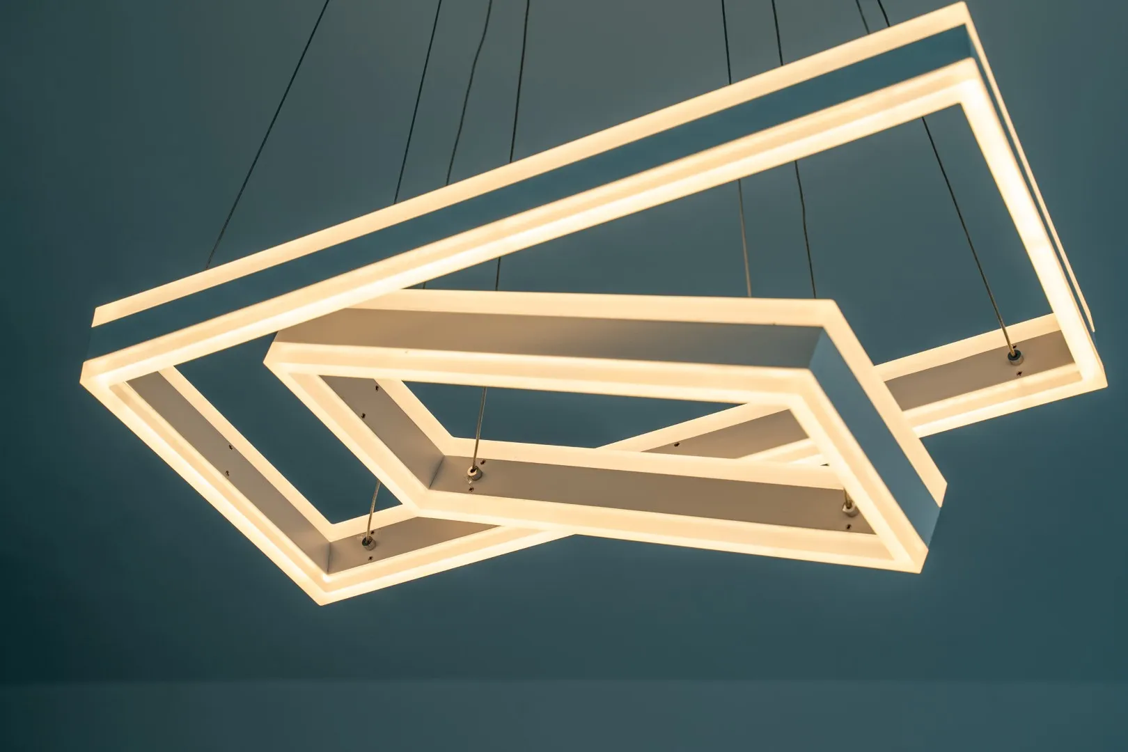 Modern geometric pendant light with warm LED illumination against a blue ceiling.