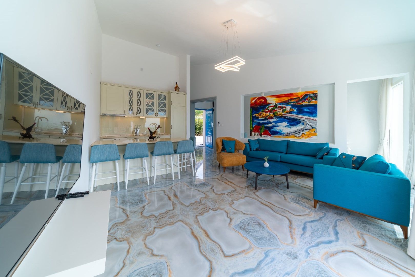 Living room with marble floor, blue furniture, and kitchen in a house, Blizikuće, Montenegro. Modern interior with a bright painting.