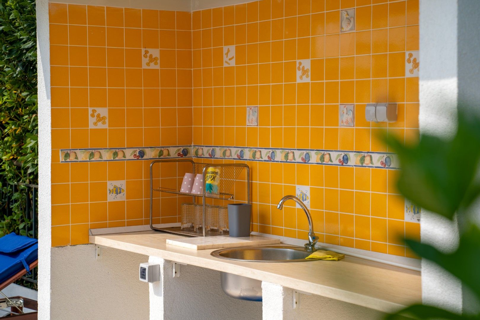 Summer kitchen with yellow tiles and a sink in a house in Blizikuće, Montenegro. Cozy outdoor barbecue area.