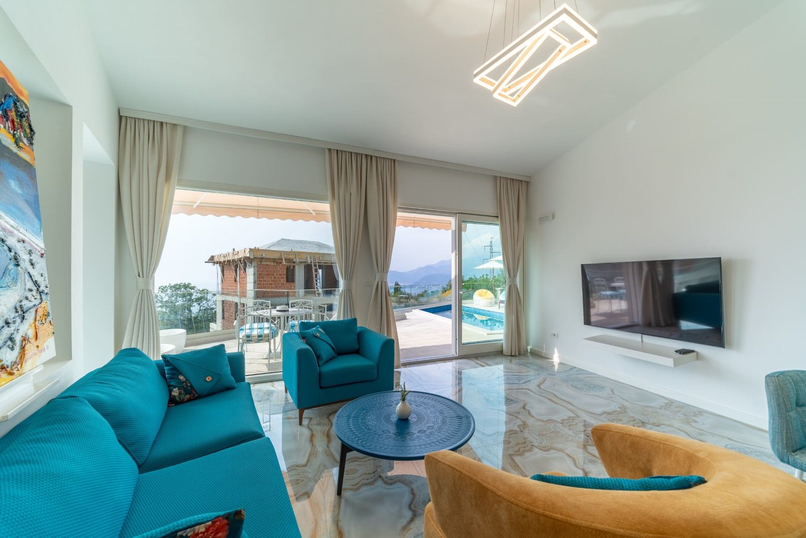 Living room in a house in Blizikuće, Montenegro: blue furniture, marble floor, panoramic windows overlooking the pool and mountains.