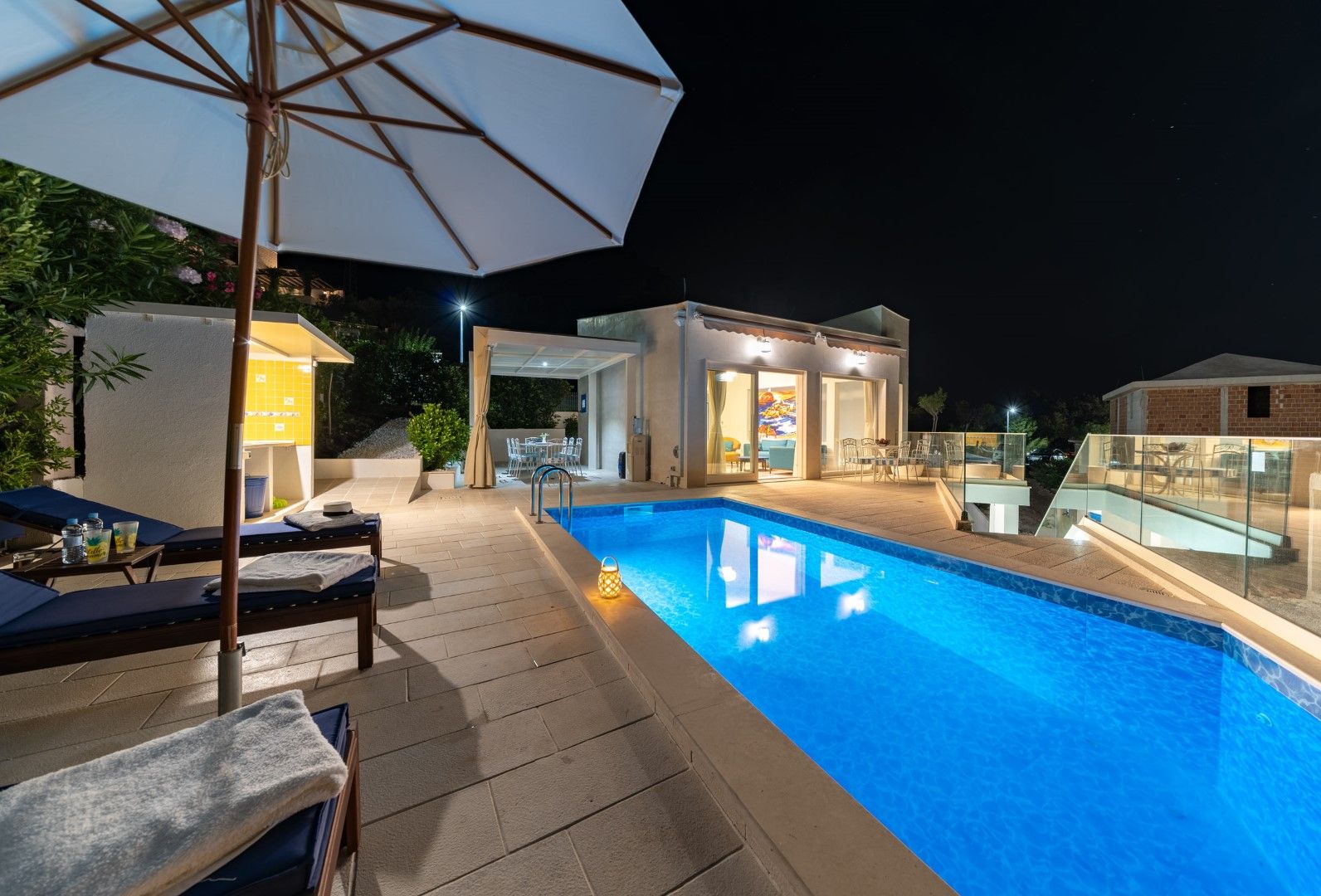 Night villa with a pool, sun loungers, and a terrace in Blizikuće, Montenegro. Modern house with lighting and a lounge area.