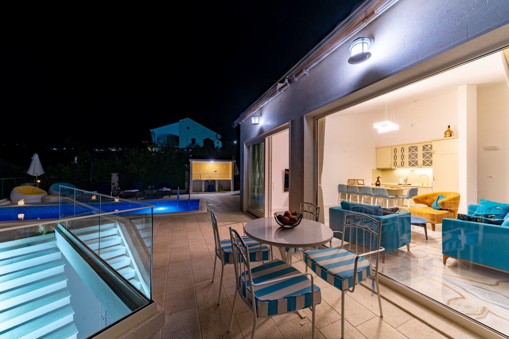 Terrace of a house in Blizikuće, Montenegro: illuminated pool, lounge area with furniture, and a panoramic view of the villa at night.