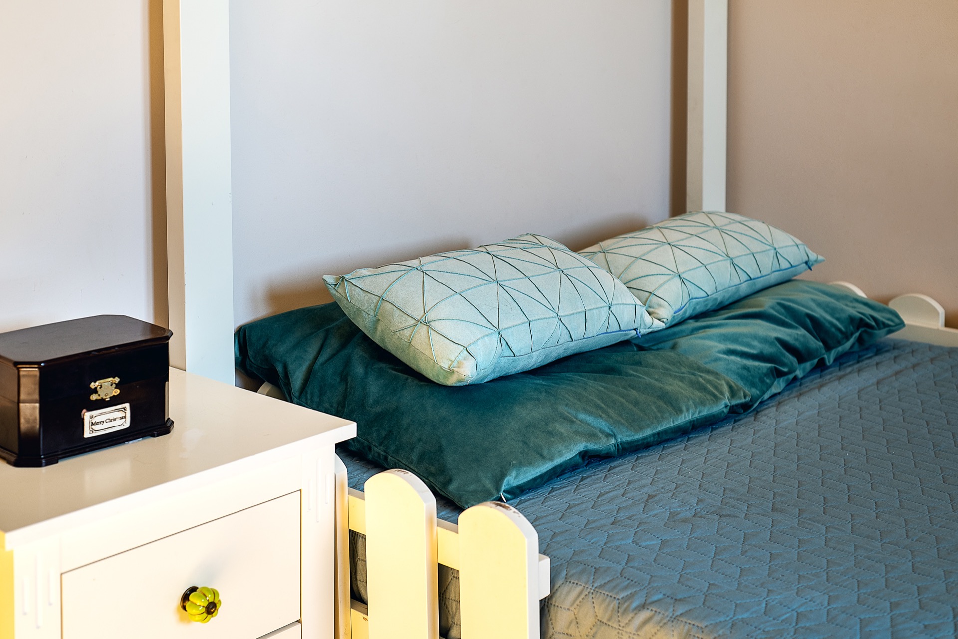 Cozy bedroom in an apartment in Budva, Montenegro: a white bed with emerald textiles and a bedside table in the interior.