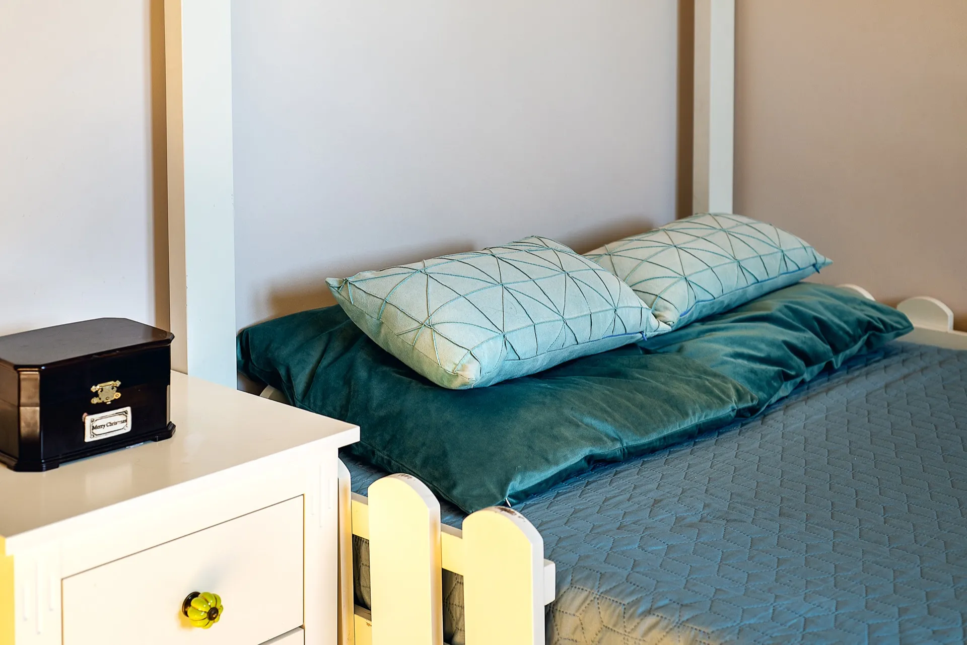 Bed with blue cover and pillows, white nightstand holding a black decorative box.