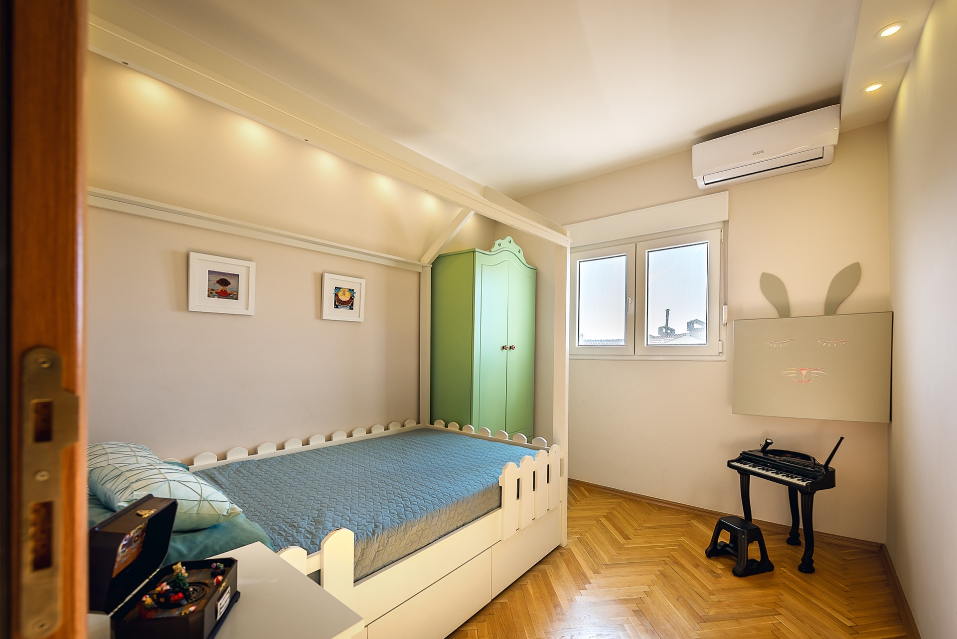 Children’s bedroom in an apartment in Budva, Montenegro: house bed, green wardrobe, parquet flooring, and air conditioner in the interior.