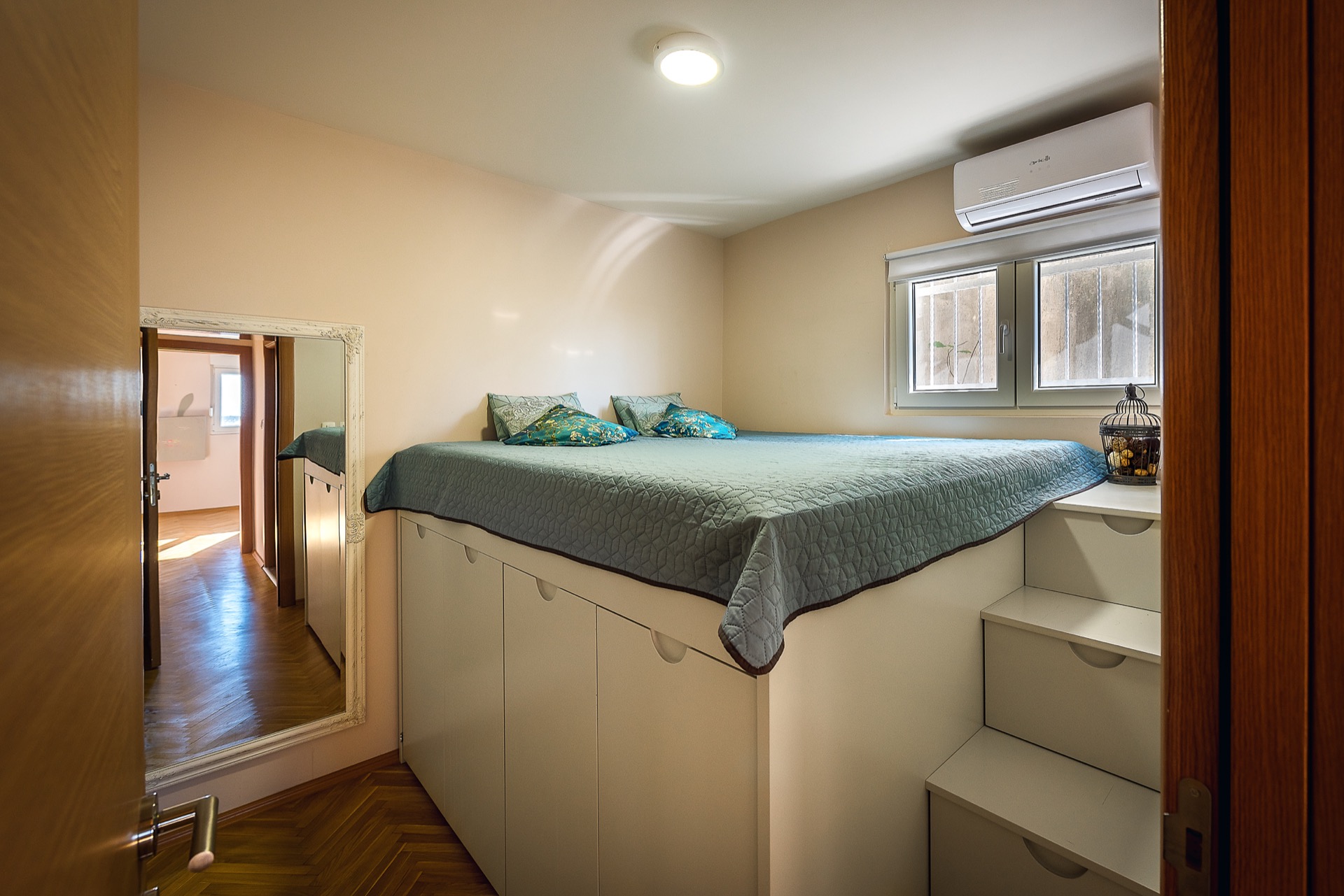 Bedroom in an apartment in Budva, Montenegro: loft bed with storage, staircase, mirror, and air conditioner.
