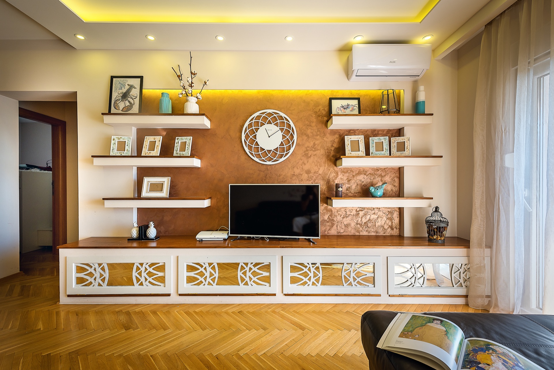 Modern living room in an apartment in Budva, Montenegro: TV area with decorative shelves, lighting, and parquet flooring.