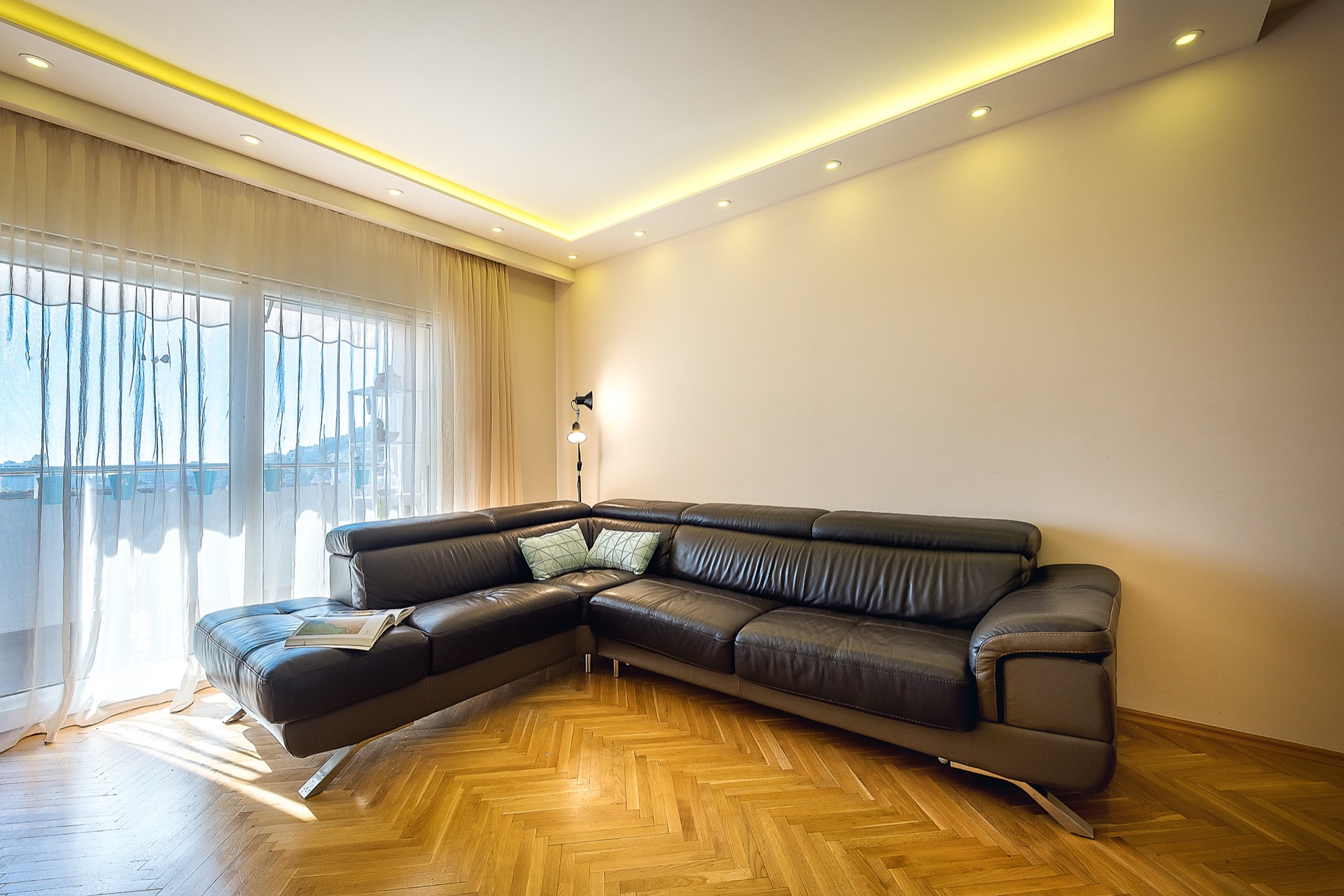 Modern living room with a leather corner sofa and parquet flooring in an apartment in Budva, Montenegro, with access to the balcony.