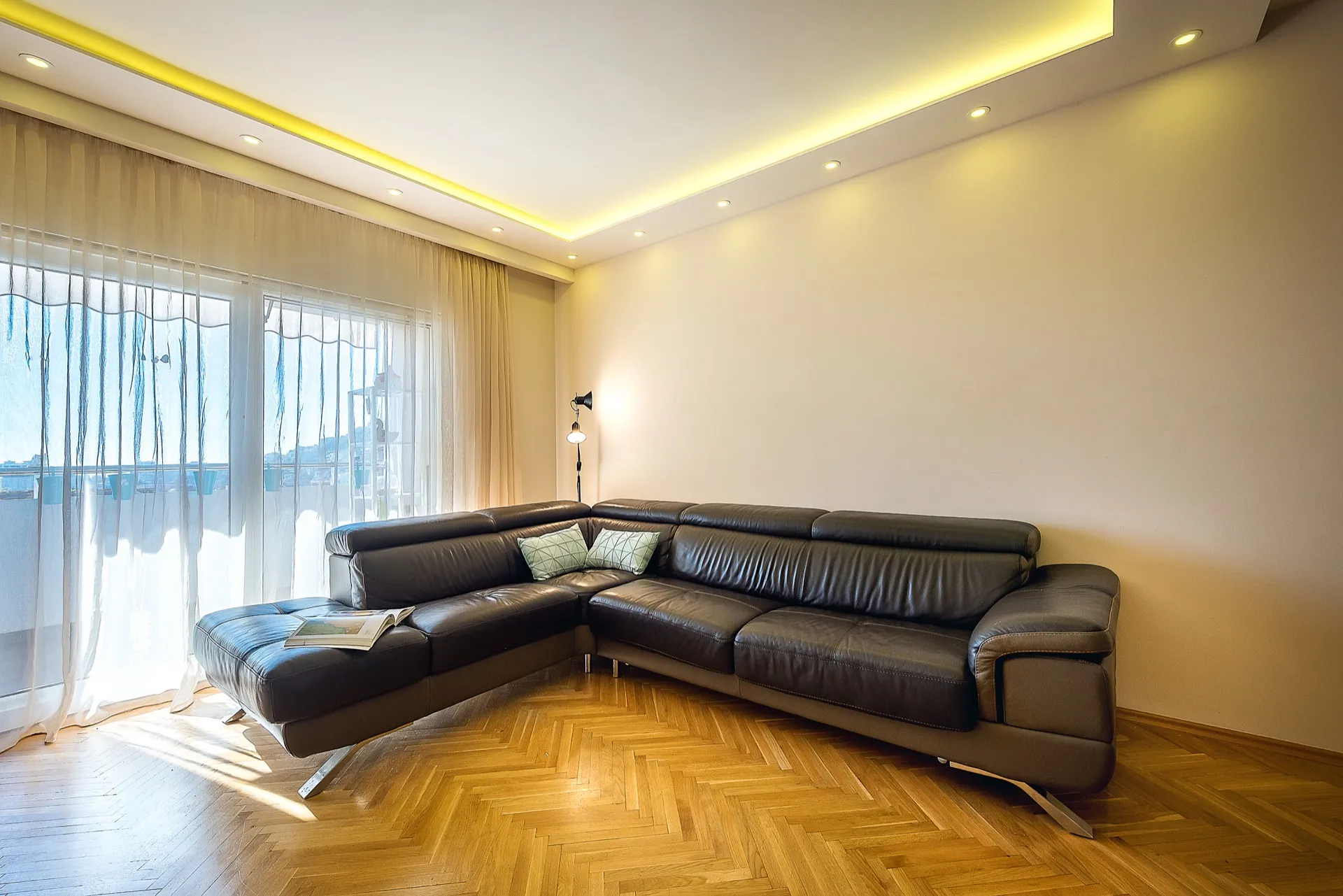 Living room featuring a large black leather sectional sofa, parquet flooring, and recessed ceiling lights.