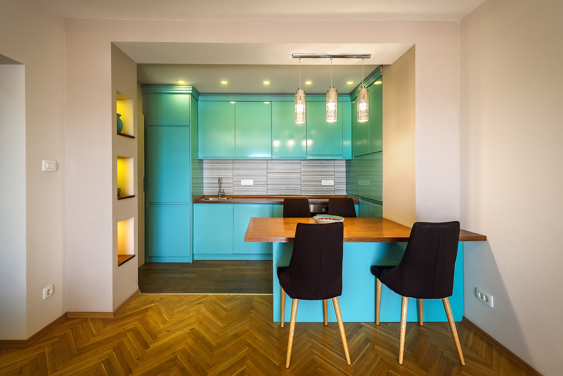Modern kitchen with a turquoise cabinet set and dining area in an apartment in Budva, Montenegro. Parquet flooring, lighting.