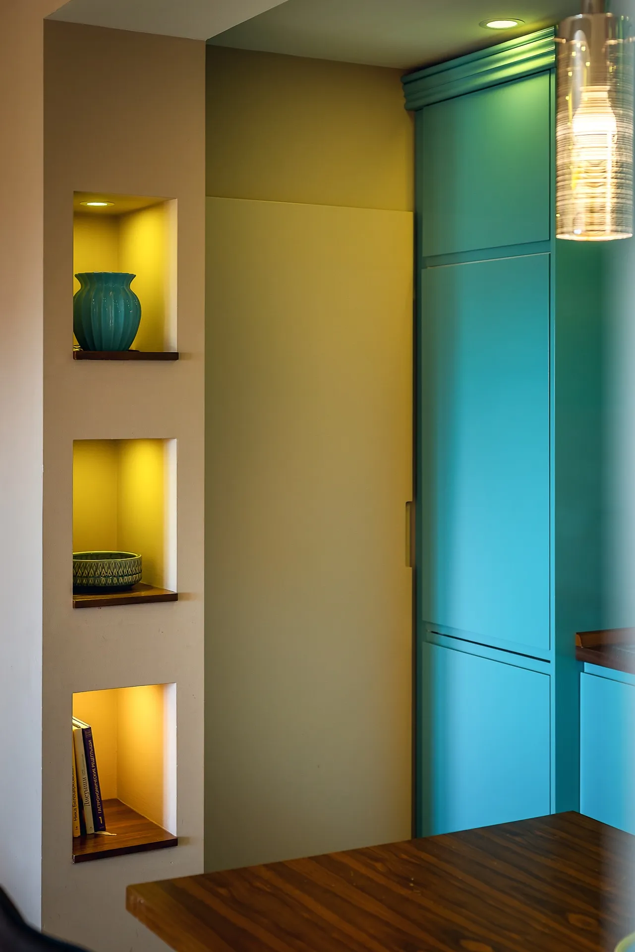 Blue cabinets, wooden table, and wall niches displaying decor and books.