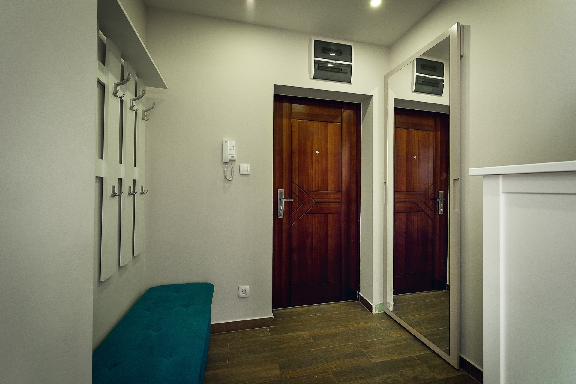 Modern hallway with a mirror, coat rack, and blue bench in an apartment in Budva, Montenegro.