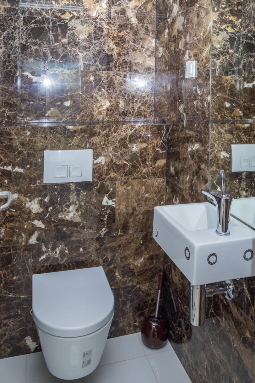 Bathroom in an apartment in Budva, Montenegro: brown marble wall finish, wall-mounted toilet, and white sink.