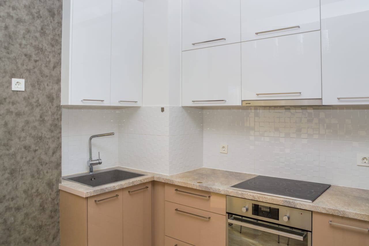 Modern kitchen in an apartment in Budva, Montenegro: white glossy cabinets, built-in appliances, and a stone countertop.