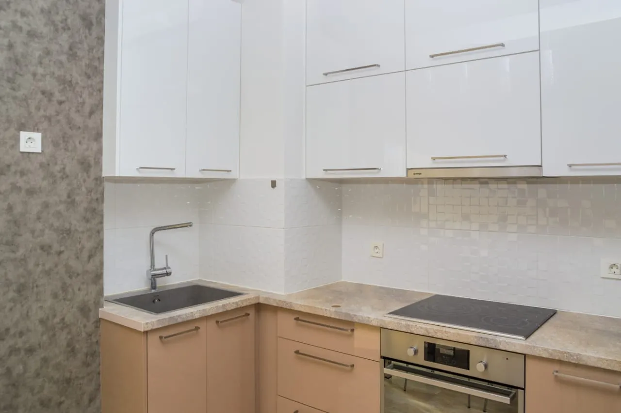 Kitchen with white upper cabinets, beige lower ones, sink, cooktop, and built-in oven against tiled backsplash.