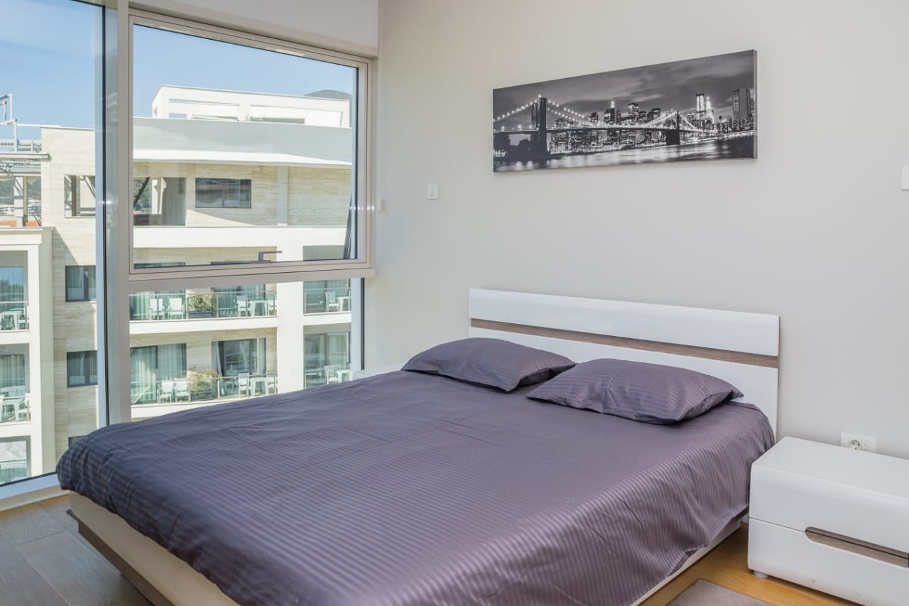 Modern bedroom with a double bed and a panoramic window in an apartment in Budva, Montenegro.