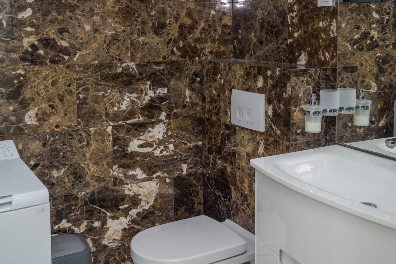 Bathroom in an apartment in Budva, Montenegro: brown marble wall finish, white fixtures, and a washing machine.
