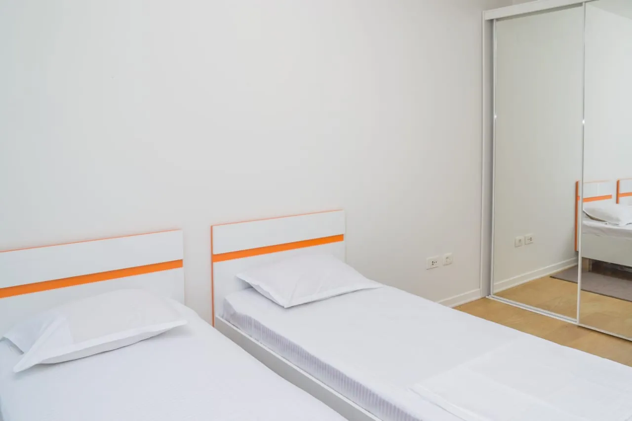 Two single beds with white bedding and orange accents on headboards next to a mirrored wardrobe.