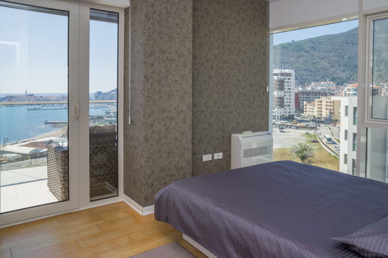 Bedroom in an apartment in Budva, Montenegro: panoramic windows with sea views, a double bed, and a modern interior.