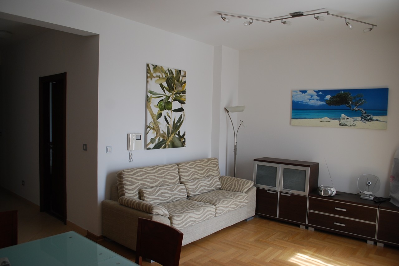 Bright living room in an apartment in Budva, Montenegro: beige sofa, wooden floor, modern furniture and decor.