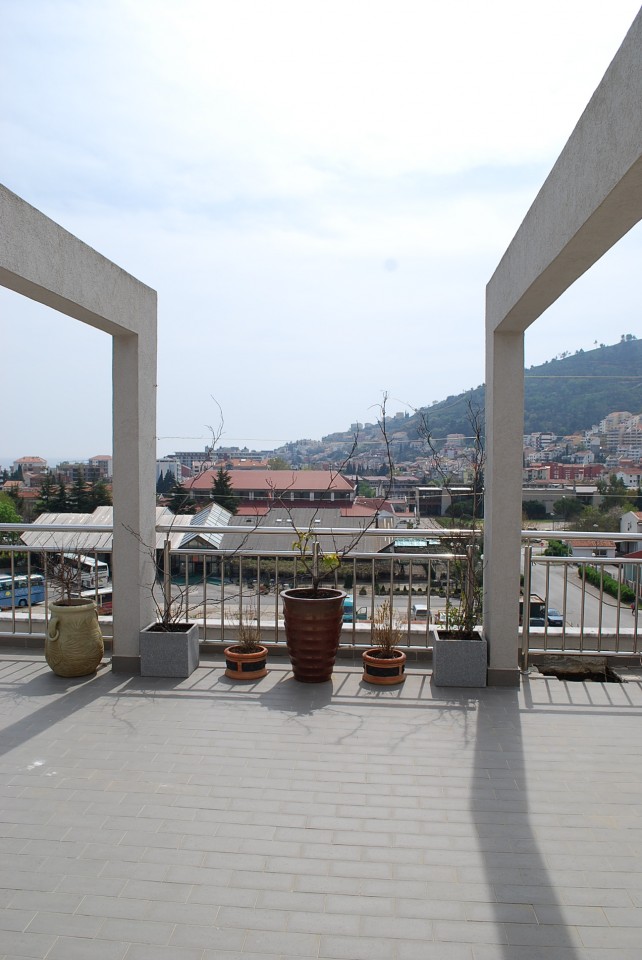 Spacious terrace with city and mountain views in an apartment, Budva, Montenegro: tiled floor and decorative plants.