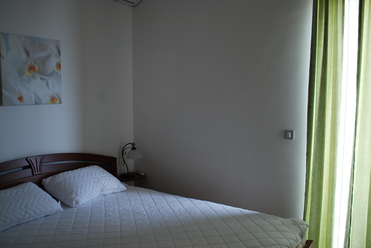 Cozy bedroom with a double bed in an apartment in Budva, Montenegro: bright interior, a painting, and green curtains.