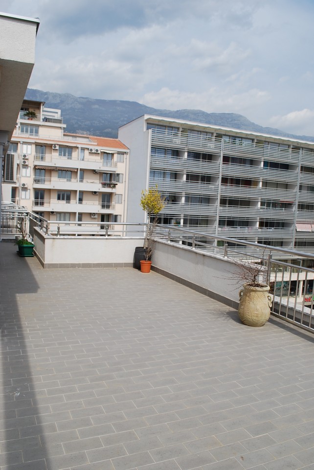 Spacious apartment terrace in Budva, Montenegro, with views of the mountains and city architecture, tiled floor, and decor.