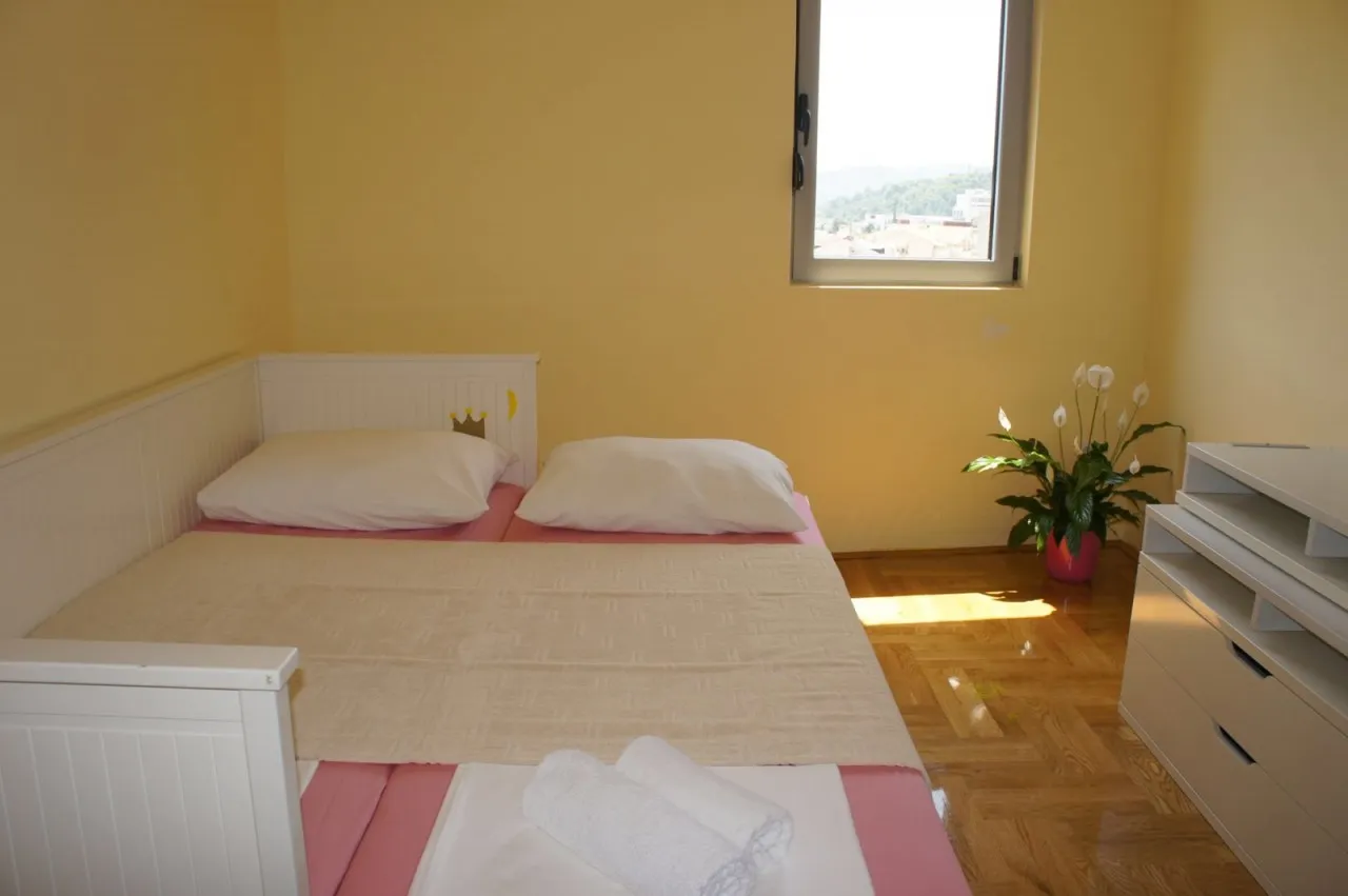 Bedroom featuring a white bed with pink bedding, a white dresser, a potted plant, and parquet flooring under natural light.