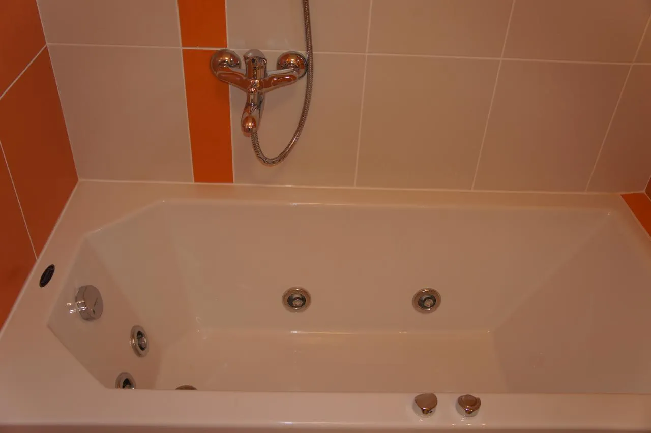 White jacuzzi bathtub with chrome fixtures and jets against beige and orange tiled walls.