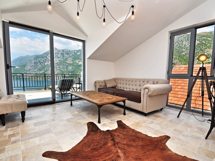 Living room in an apartment in Risan, Montenegro: panoramic view of the Bay of Kotor, designer furniture, and stone flooring.
