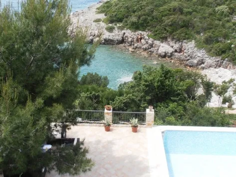 Terrace with a swimming pool and railing overlooking a rocky coastline and turquoise sea water.