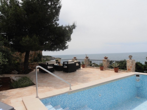 Terrace with a pool and sea view at a villa in Luštica, Montenegro: wicker chairs, stone finishes, and landscaping.