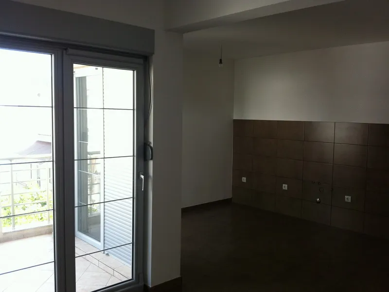 Empty room with dark floor tiles and a tiled wall section containing electrical outlets and water pipe connections next to a large glass door.