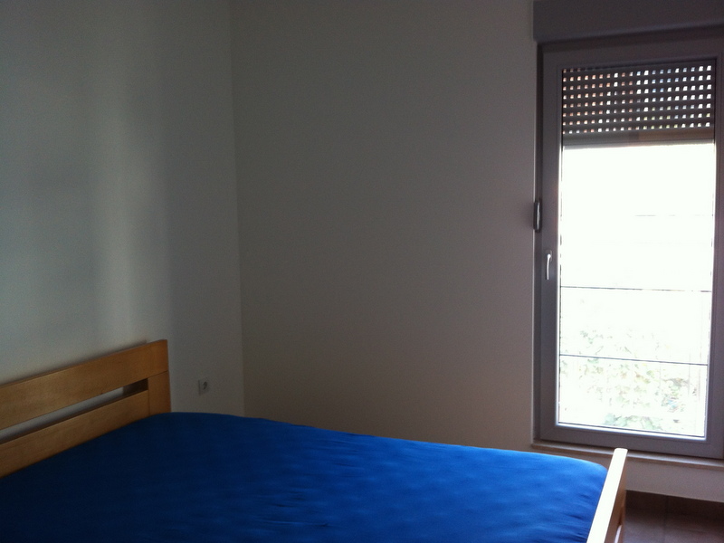 Bedroom in an apartment in Petrovac, Montenegro: a wooden bed with a blue bedspread and access to a balcony with roller shutters.