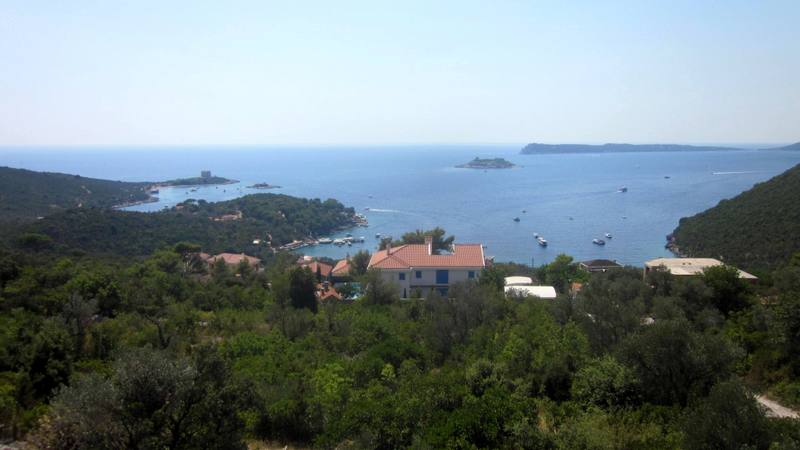 Panoramic view of the sea and Žanjice Bay, Montenegro, from a plot of land surrounded by greenery and Mediterranean mountains.