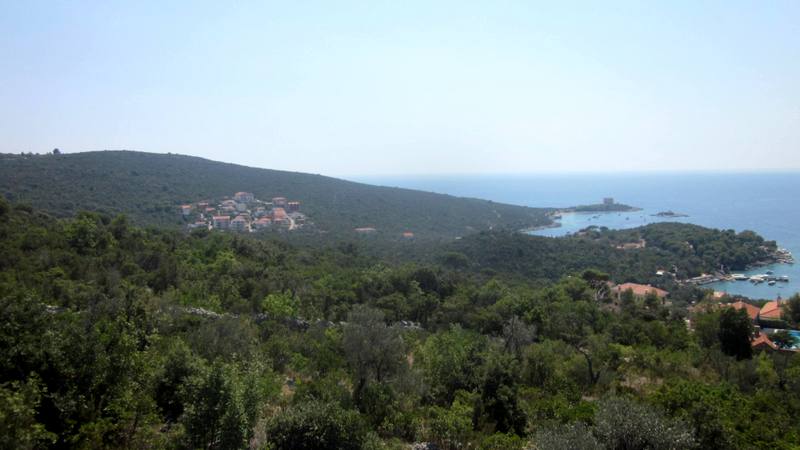 Panoramic view of the sea and the Žanjice coast, Montenegro: a plot of land surrounded by greenery and hills.