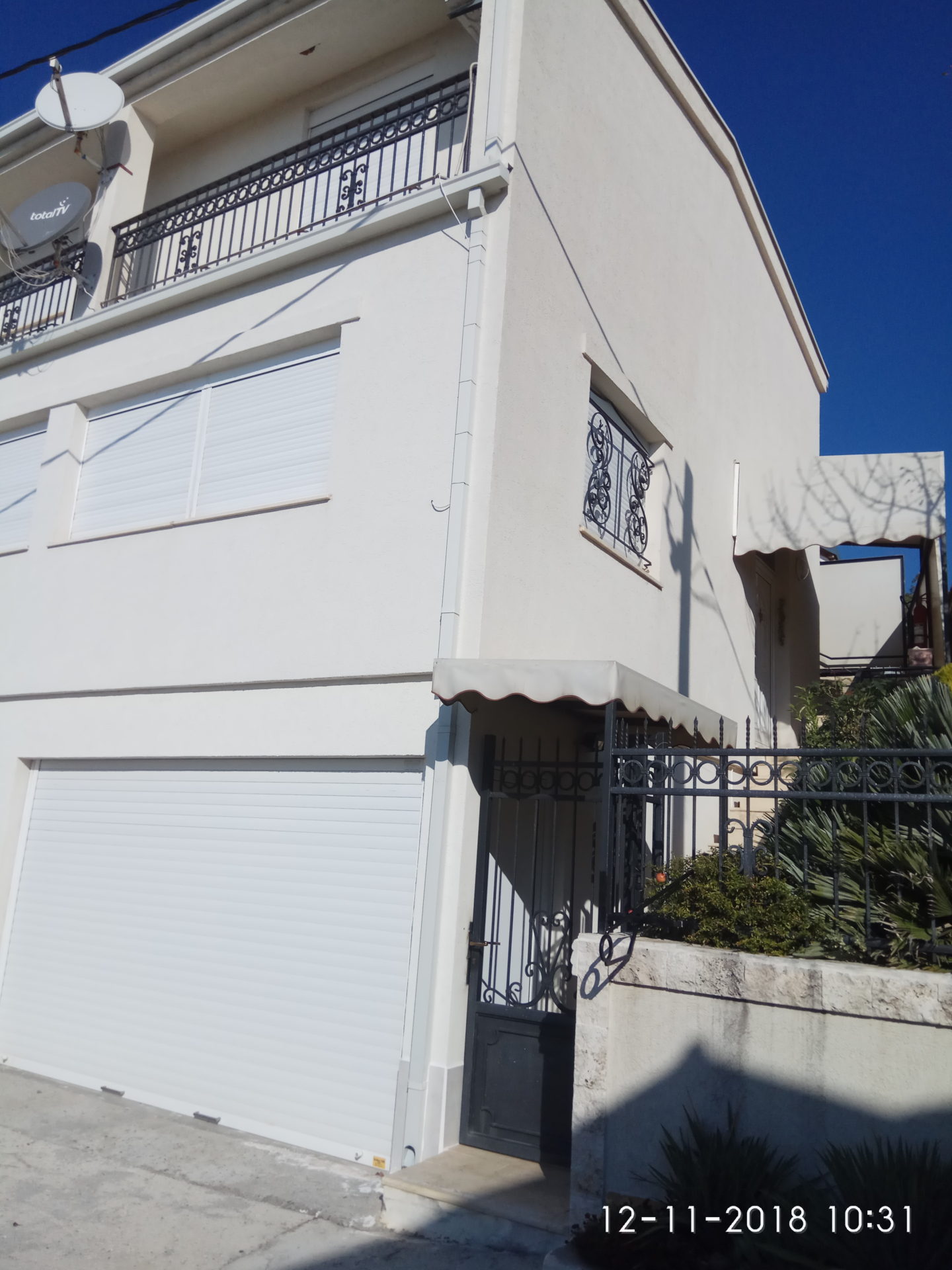 Facade of a two-story house in Ratac, Bar Riviera, Montenegro: garage with roller shutters, wrought-iron railings, and a terrace.