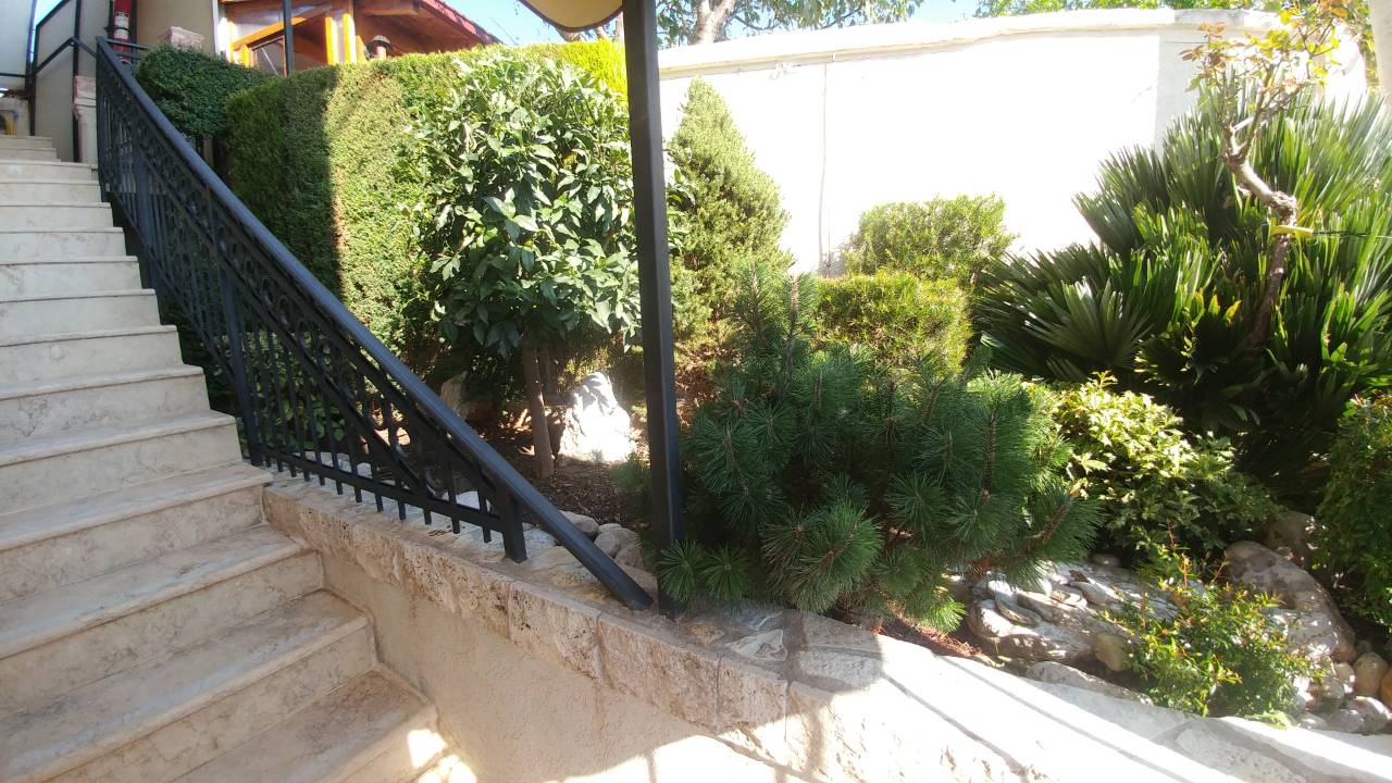Stone staircase with wrought-iron railings in the garden of a house in Ratac, Bar Riviera, Montenegro, surrounded by coniferous trees.