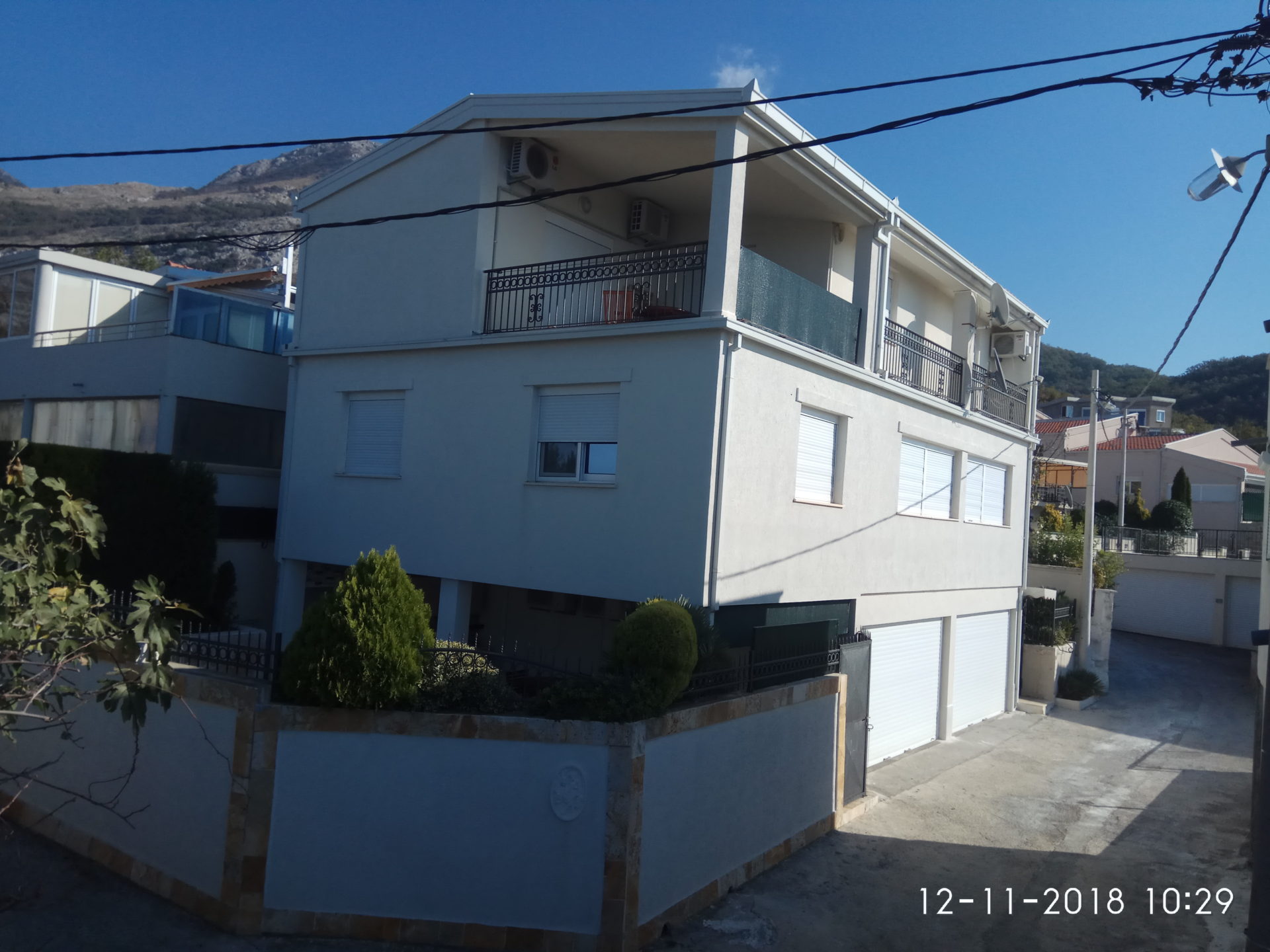 Three-story house in Ratac, Bar Riviera, Montenegro: facade with balconies, garage doors, and mountain views.