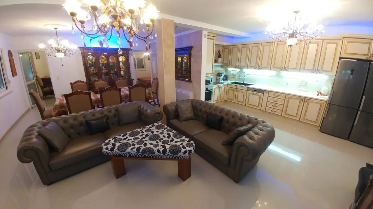 Living room with brown leather sofas, patterned coffee table, and visible kitchen area in background.